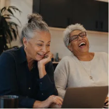 Two women laughing together over a laptop.